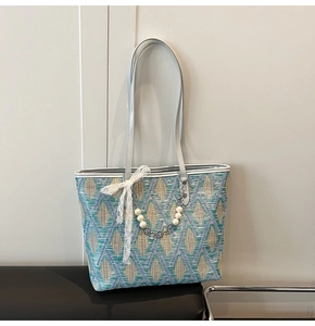 Detail of woven tote bag with green diamond pattern, pearl charm and lace bow