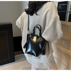 Detail of a black patent leather bucket bag featuring a high-gloss finish and adjustable strap