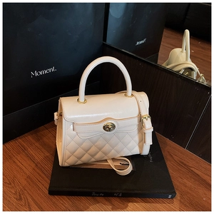 Détail d'un sac matelassé blanc crème avec fermoir doré sur un fond esthétique sombre