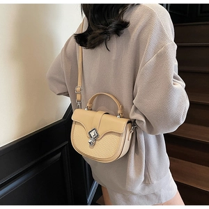 Détail d'un sac selle bicolore avec texture tissée beige et boucle en métal dorée