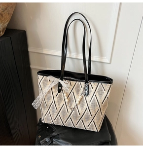 Detail of woven beige and black tote bag with white lace bow and pearl pendant