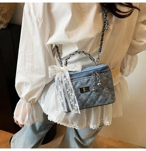 Detail of blue denim box bag featuring quilted pattern and white lace bow decoration