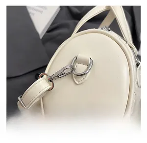 Détail du crochet en métal argenté et de la bandoulière en cuir blanc sur un sac cylindre