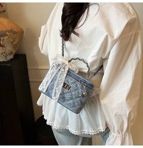 Detail of blue denim quilted box bag with lace bow and chain strap on a model