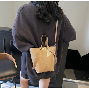 Detailed view of khaki bucket bag with wing-shaped handle and silver rivet hardware detail