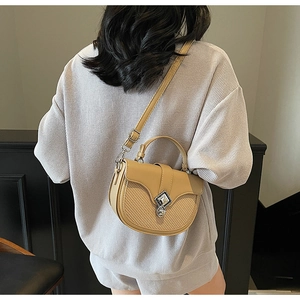 Détail du sac selle beige bicolore avec boucle argentée et texture tissée élégante