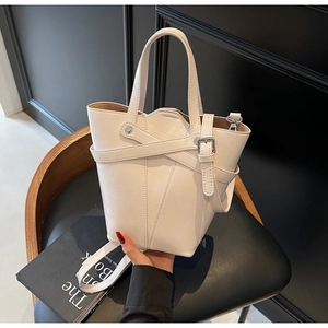 Detail of off-white bucket bag featuring cross-strap design and silver-tone metal buckles