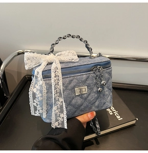 Detail of blue denim quilted box bag with a white lace bow and silver chain handle