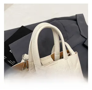 Gros plan du sac à main blanc en cuir grainé avec fermoir rotatif argenté et double poignée