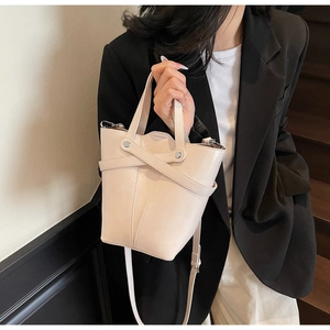 Detail of a beige bucket bag with silver studs and adjustable strap on a black blazer