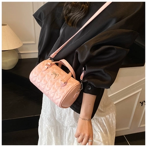 Détail d'un sac polochon rose avec matelassage en cœur et breloque nœud doré élégant