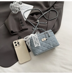 Detail of blue denim quilted bag featuring lace bow, gold twist lock, and chain strap