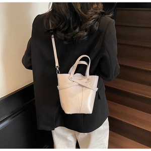 Chic cream bucket bag with cross-strap detail shown on model against wooden background