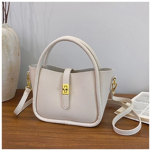 Detail of white lychee leather mini bucket bag with gold lock on a minimalist desk