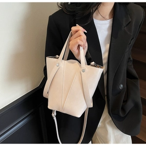 Close-up of cream bucket bag showing geometric stitching and silver rivet hardware details