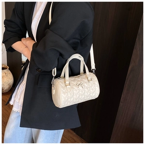 Détail du sac tonneau crème avec surpiqûres en cœur, nœud décoratif et bandoulière