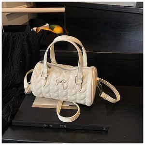 Détail du sac tonneau crème avec matelassage cœur et nœud argenté sur fond noir