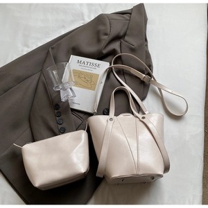 Detail view of beige bucket bag set with inner pouch and metal feet on white fabric