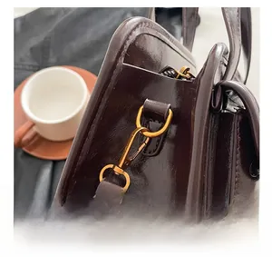 Detail showing polished gold hardware hooks and dark brown glossy leather on a handbag