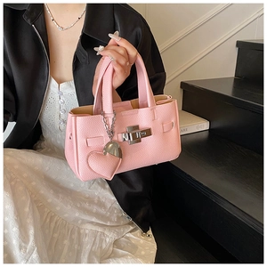 Détail d'un sac à main en cuir rose avec fermoir rotatif argenté et pendentif cœur