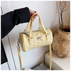 Détail du sac cylindrique jaune clair matelassé cœur avec boucle nœud métallique