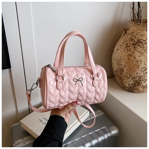 Détail du sac cylindrique rose avec matelassage en cœur et nœud argenté élégant