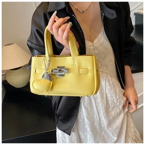 Détail d'un sac à main jaune en cuir avec fermoir argenté et breloque en cœur