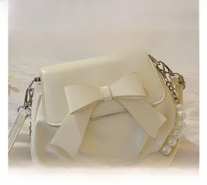 Detail of cream-white patent leather bag with a large bow and elegant pearl chain strap