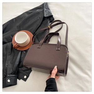 Detailed view of deep brown glossy rectangular handbag with gold hardware on beige fabric