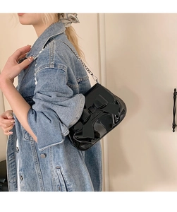 Detail of black patent leather crossbody bag with bow decoration and silver chain strap