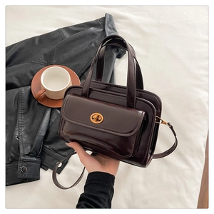 Detailed close-up of dark brown glossy leather handbag with gold clasp and top handle