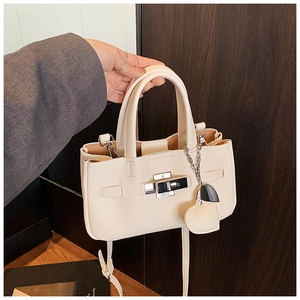 Détail d'un sac à main en cuir beige grainé avec fermoir tournant et breloque en cœur