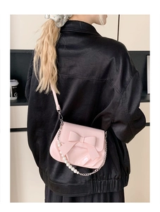 Detail of pink patent leather crossbody bag with bow and pearl chain on a black coat