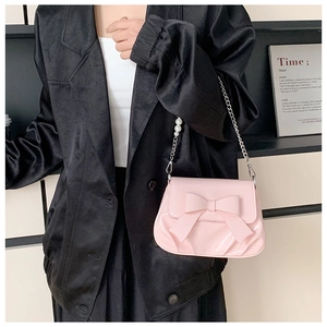 Detail of pink patent leather handbag with a large bow and pearl chain strap accents