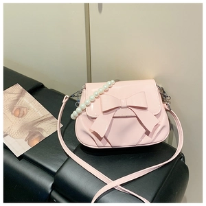 Close-up of pink patent leather crossbody bag featuring a large bow and pearl handle