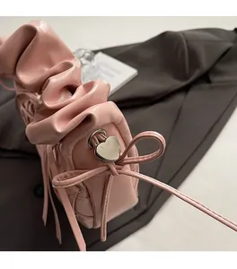 Détail du sac bandoulière plissé rose avec un nœud et un pendentif cœur en métal