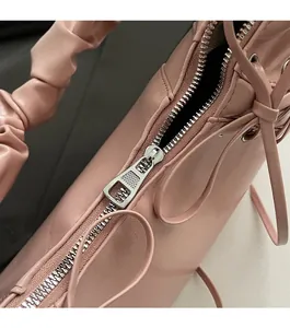 Détail de la fermeture éclair en métal argenté et de la bandoulière plissée rose du sac
