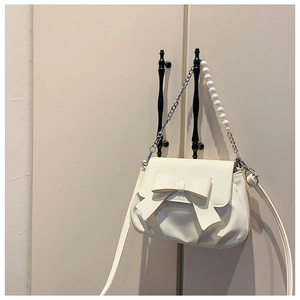 Detailed view of white patent leather crossbody bag with oversized bow and pearl chain