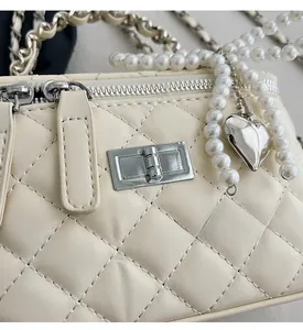 Detail of beige quilted chain bag featuring silver turn-lock and pearl heart pendant