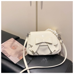 Macro view of white patent leather shoulder bag with bow and pearl chain handle