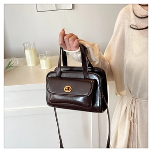 Detail of vintage chocolate brown glossy leather handbag with elegant gold metal twist lock