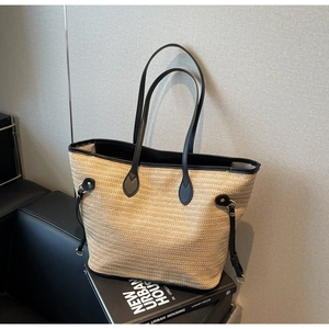 Detail of woven straw tote bag featuring black leather handles and adjustable side drawstrings
