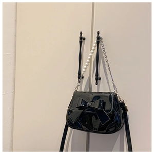 Detail of black patent leather crossbody bag with a large bow and pearl chain strap