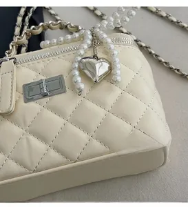 Detail of cream quilted bag with silver heart charm and faux pearl strap close-up