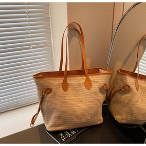 Close-up of woven straw tote bag featuring brown leather handles and side drawstring detail