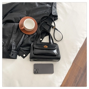 Close-up of black leather handbag featuring golden twist lock and adjustable shoulder strap