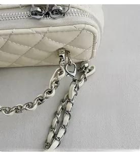 Detail of white quilted crossbody bag with silver hardware hooks and chain strap