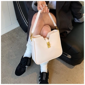 Detail of minimalist cream leather handbag featuring a gold buckle and V-shaped design