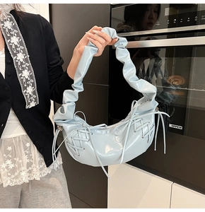 Détail du sac croissant bleu clair brillant avec bandoulière froncée et nœuds latéraux