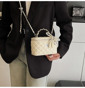 Detail of off-white quilted crossbody bag with pearl handle and bow charm on a model